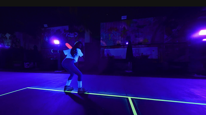 a person plays pickleball under blacklights
